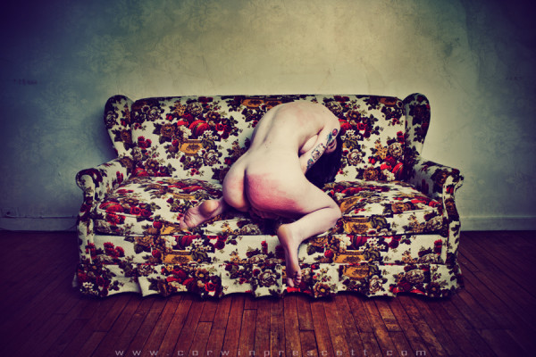 Femme nue, assise de dos sur un canapé fleuri, cul rougi