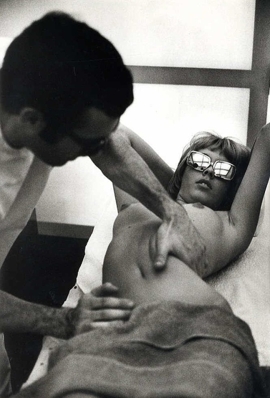 Une femme, lunettes de soleil, poitrine nue, se fait masser par un professionel
